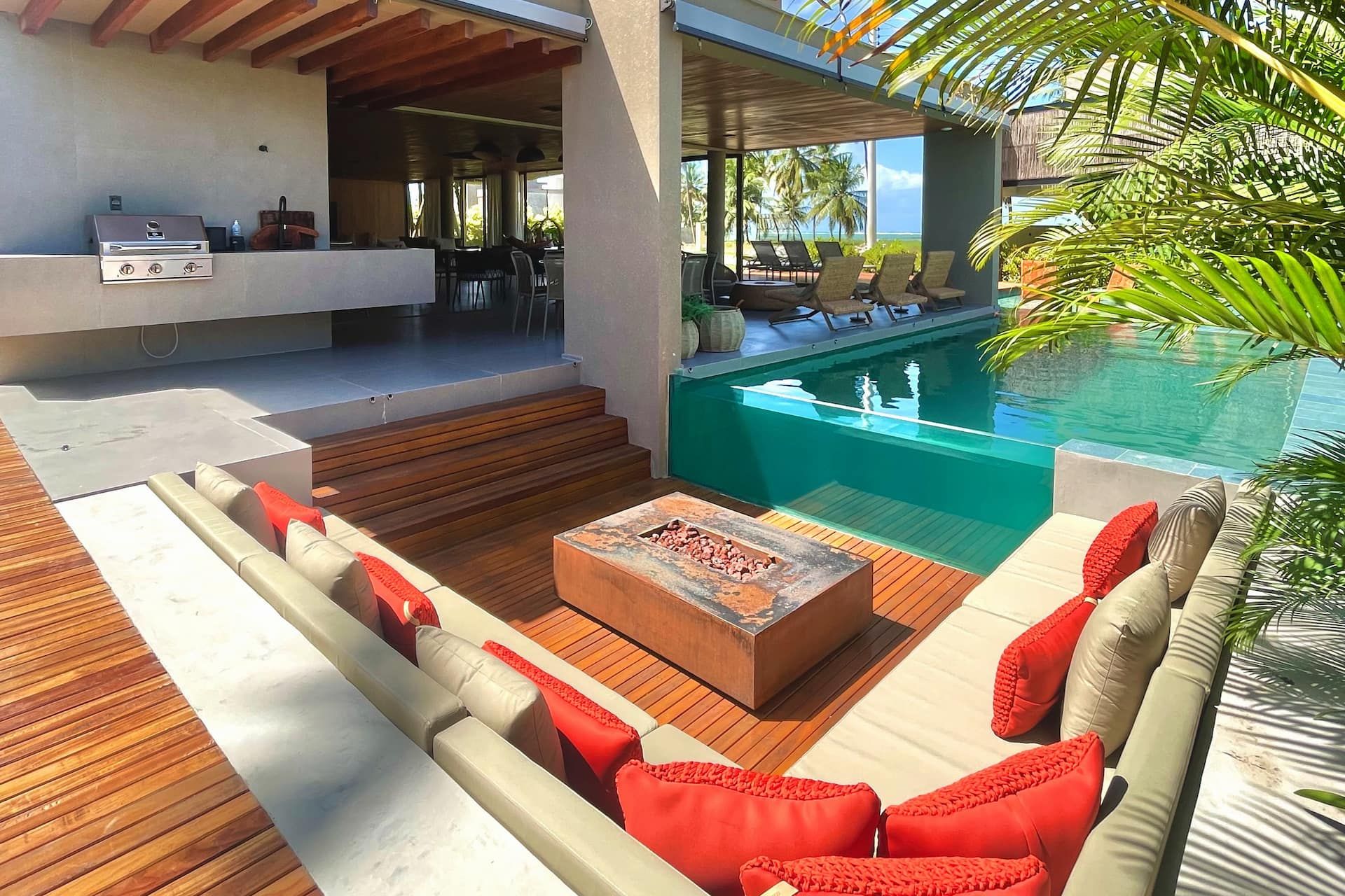 Lounge externo com lareira acesa, almofadas vermelhas e a piscina da Casa Pérola ao lado