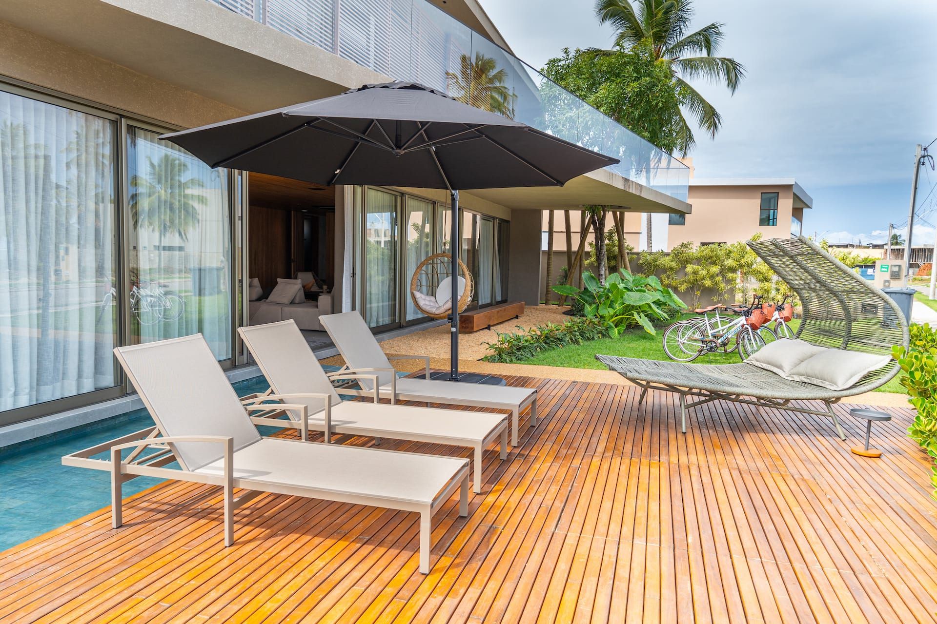 Deck de madeira da piscina com espreguiçadeiras, guarda-sol e rede suspensa