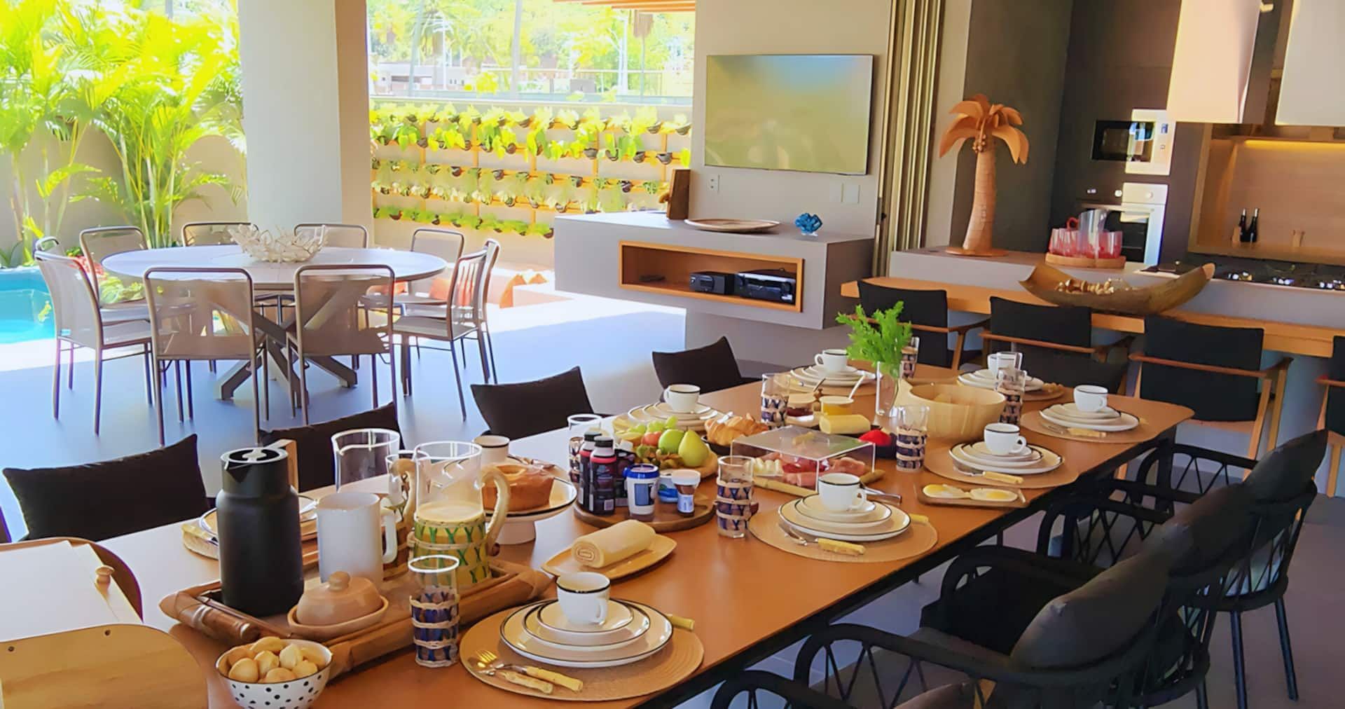 Mesa longa posta para o café da manhã preparado pela equipe da casa, com a piscina ao fundo
