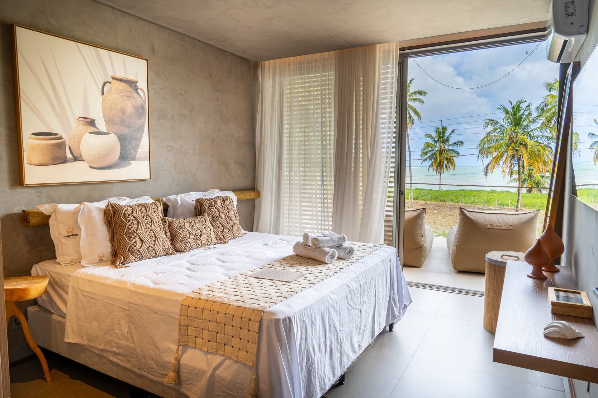 Suíte com cama de casal, poltrona de leitura e janela ampla voltada para os coqueiros