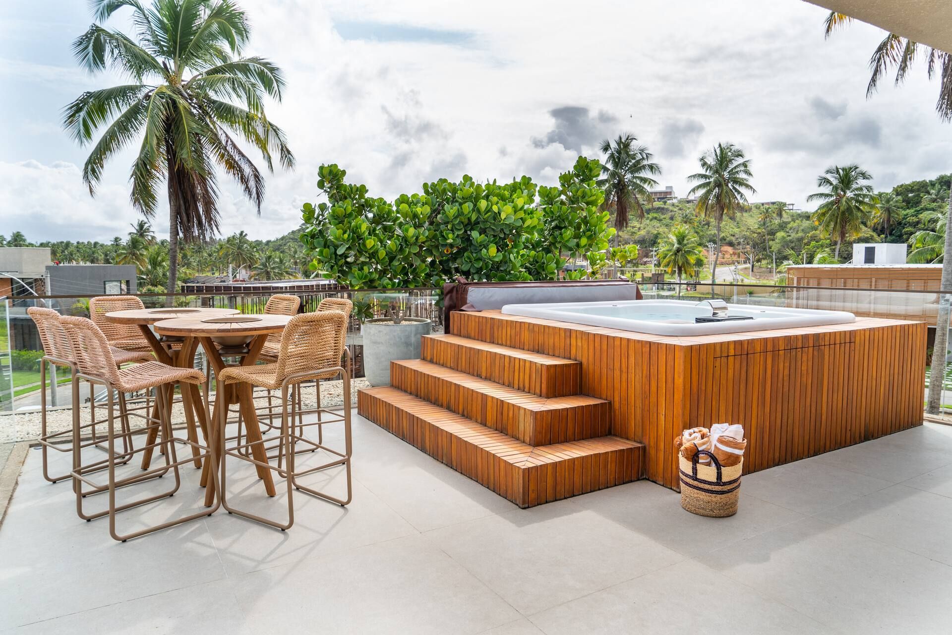 Rooftop da Casa Pérola com hidromassagem revestida em madeira e mesa bistrô alta entre os coqueiros