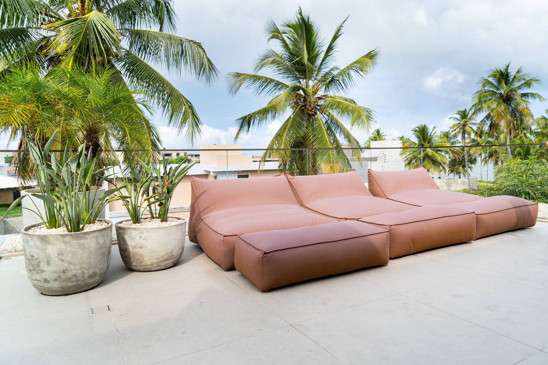 Sofá modular terracota no rooftop, com vasos de plantas e coqueiros ao fundo