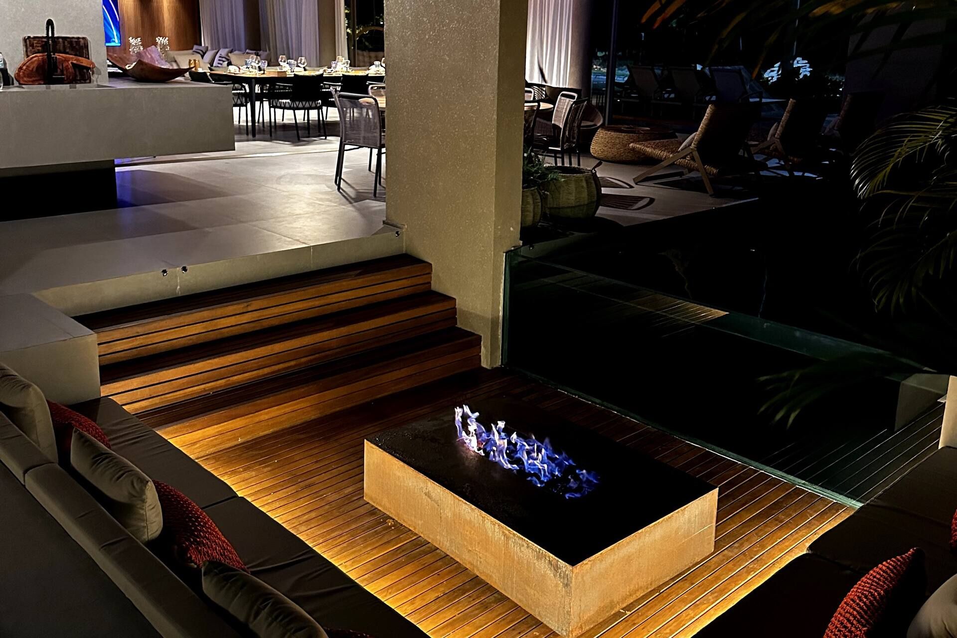 Lareira externa acesa à noite junto ao deck, com a piscina iluminada da Casa Pérola ao fundo