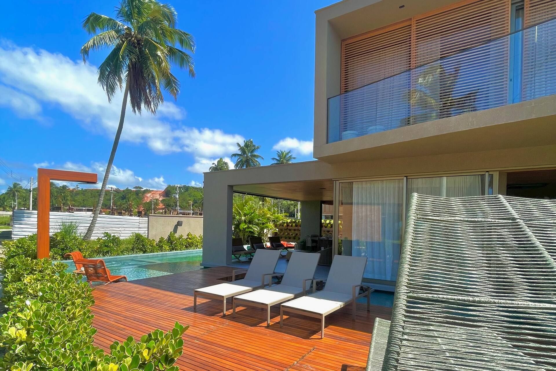 Fachada lateral da Casa Pérola com deck, espreguiçadeiras e um coqueiro inclinado sobre a piscina